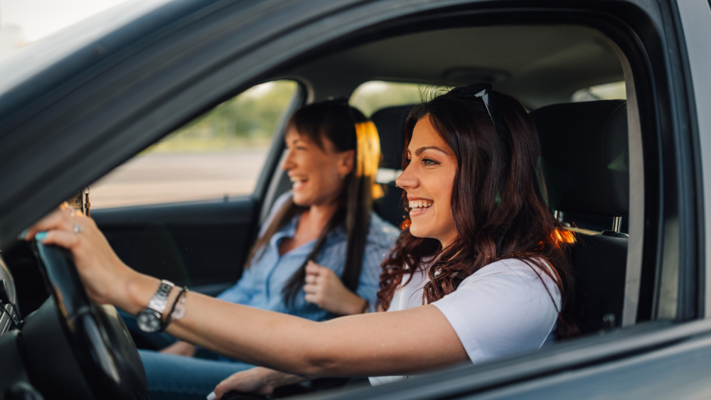 Two women driving a car and smiling