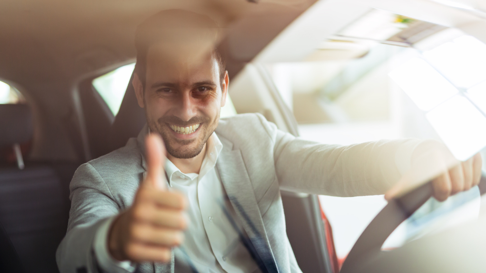 Uomo sorridente alla guida di un'auto con il pollice in su