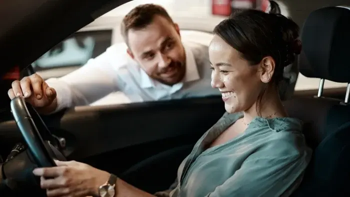 Woman smiling in car with dealership service agent 